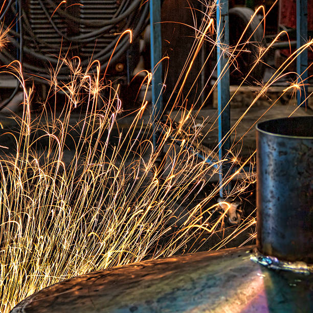 Photograph of an industrial workshop where a worker is cutting metal with an angle grinder, generating a shower of bright sparks around the metal piece.