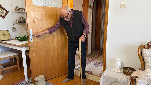 Senior man with a walking with cane and holding doorknob stick at home
