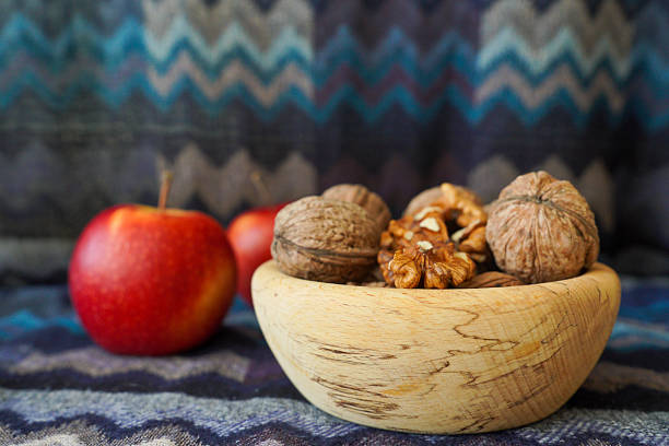Walnuts and walnut kernels in a wooden bowl with red apples in the background. Rustic still life food photography, healthy nutrition concept, natural organic ingredients.