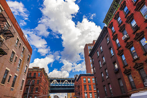 New York. USA.   September 20.2022. Beautiful upward view between historic Manhattan buildings toward bright blue sky with white clouds and elevated walkway.