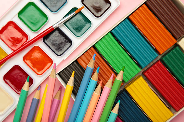 Colored pencils, plasticine and watercolor paints on pink background. Top view