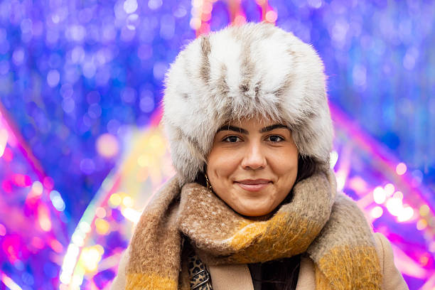 A young woman in warm seasonal clothing smiles naturally in an urban setting.