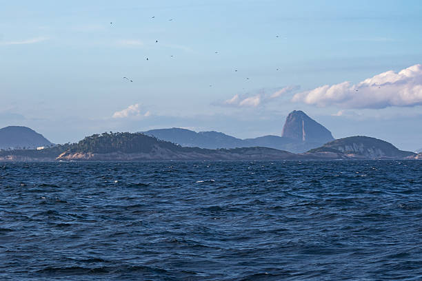 This scenic coastal view features deep blue ocean waters leading toward a series of distant mountain formations under a clear sky. Its calm atmosphere and natural beauty make it a popular choice for travel themes, maritime concepts, outdoor inspiration, and scenic landscape imagery.
