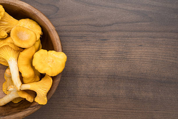 Raw fresh golden chanterelles edible mushrooms before being cooked. Yellow chanterelles in bowl on brown wooden background with copy space.