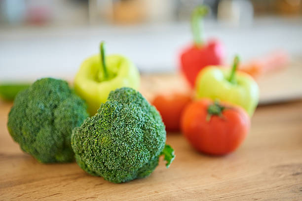 Fresh broccoli florets, vibrant red and green bell peppers, and ripe red tomatoes are arranged on a light wooden cutting board, symbolizing healthy eating and a balanced diet