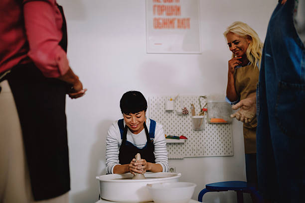 A diverse group of women participating in a pottery class, learning to shape clay on the pottery wheel in a creative studio setting. The image highlights hands-on learning, cultural diversity, and the joy of artistic exploration. Ideal for concepts such as creative workshops, art education, community learning, female empowerment, and multicultural collaboration.