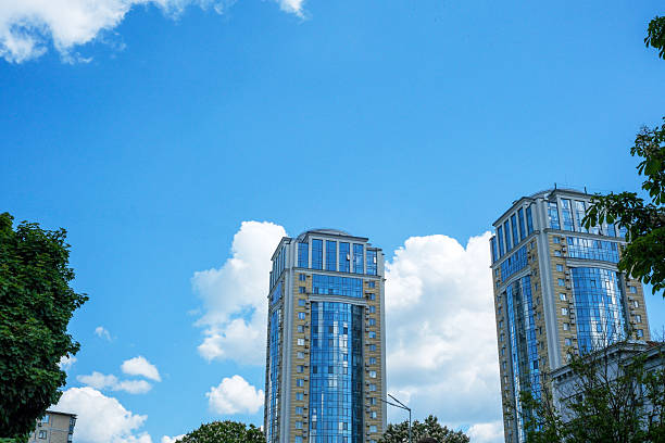 Tall buildings showcase reflective glass panels under a vivid azure sky and white clouds.