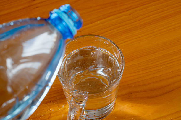 Cold water cascades from a bottle into a transparent glass on a table.