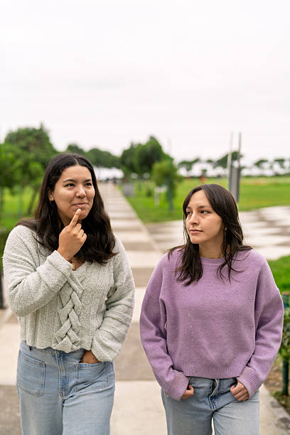 Two young adult friends enjoying a leisurely walk in a park, engaging in conversation while reflecting on thoughts