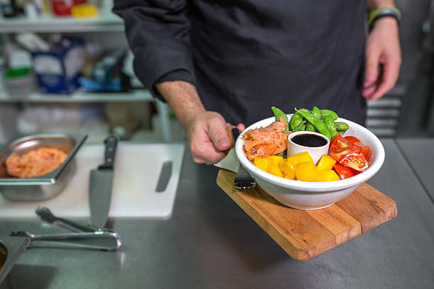 Unrecognizable chef with apron showing fresh colorful poke bowl with salmon on restaurant kitchen