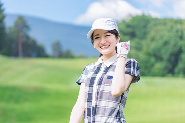close-up candid portrait of an Asian woman in a white cap and bright orange golf attire, smiling joyfully beside a golf cart. Captured in natural light on a lush green course, symbolizing active lifestyle, outdoor leisure, and positive energy.