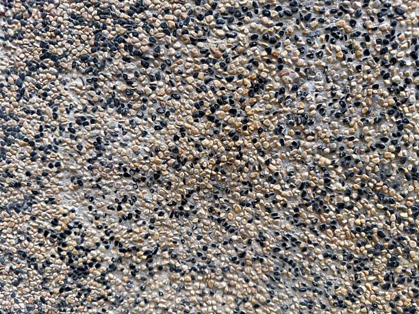 Abstract close-up texture of pebble stone floor with black and beige small stones embedded in cement, rough natural surface background suitable for architecture, construction, and design use.