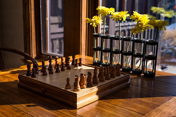 Quality chess board with chess pieces on table with natural window light filtering in.