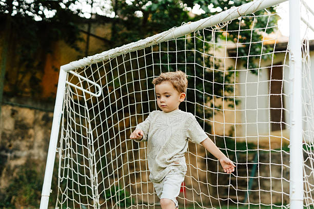 Goalie defending his nets as he dives down while team member kick the ball. Net is in focus and soccer players are blurred
