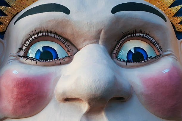 Tight crop of a large, stylized face with bright blue eyes, long eyelashes, and rosy cheeks from an amusement park entrance.
