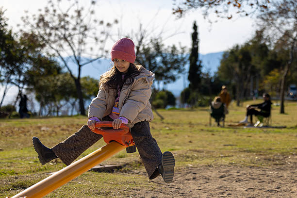 Young girl enjoying a sunny day at the playground, riding a wooden seesaw.