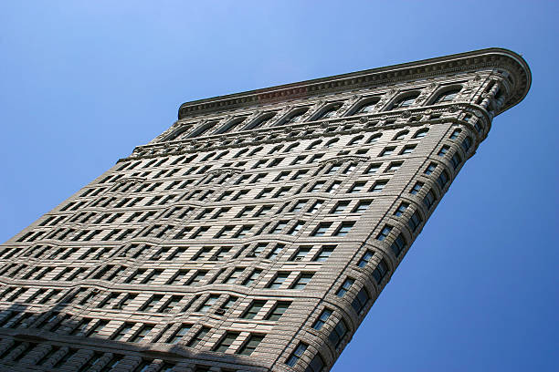 Side perspective of the Flatiron Building stretching diagonally across the frame with a clear blue sky backdrop.