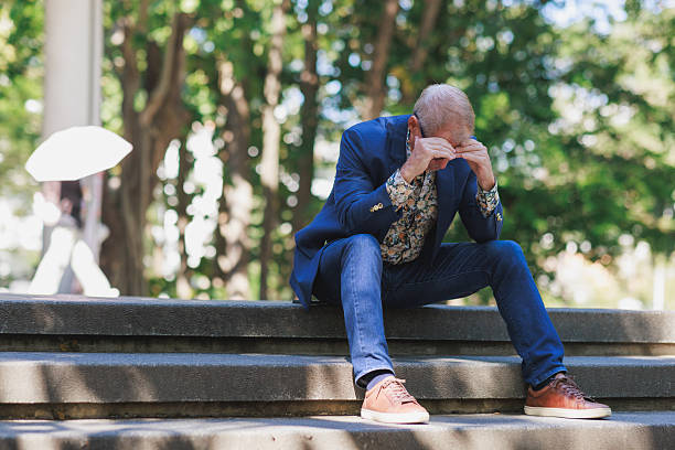 Mature man covering his face with hands, experiencing stress, depression, or emotional pain outdoors