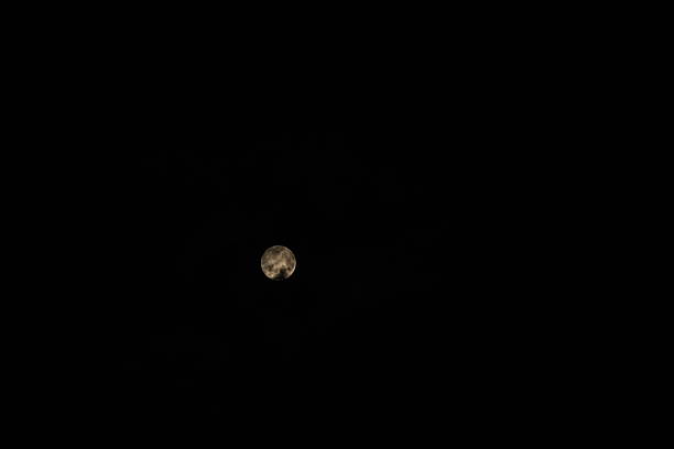Full moon glowing in the darkness of the night sky with subtle cloud cover