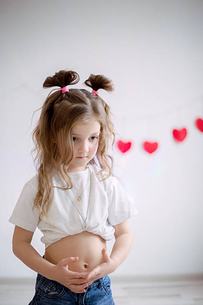 Happy young girl expressing herself through energetic dance movements against white wall decorated with festive red hearts, celebrating Valentine's Day with joy and carefree playful spirit