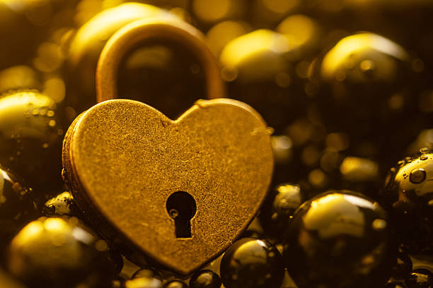 A golden heart with a keyhole in the middle. The heart is surrounded by many small, shiny, round beads. Concept of warmth and love, as the heart is a symbol of affection