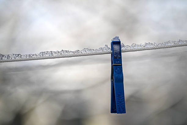 A blue clothespin is hanging on a clothesline. The clothespin is frozen in ice. Concept of coldness and stillness