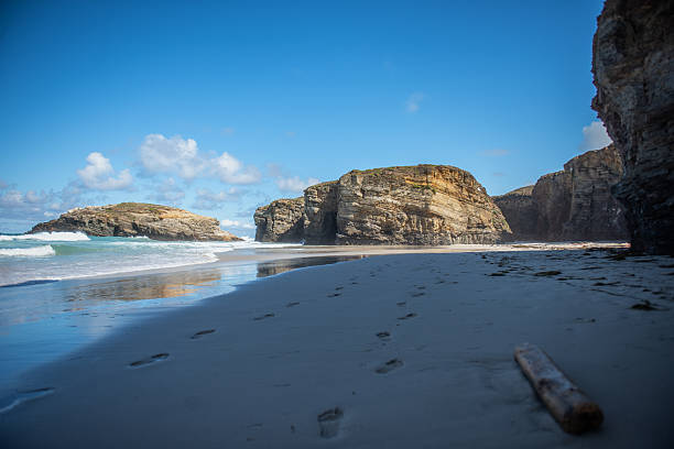 Majestic rocky cliffs on empty sandy beach under blue sky, luxury resort marketing or nature conservation. Spain. Galicia