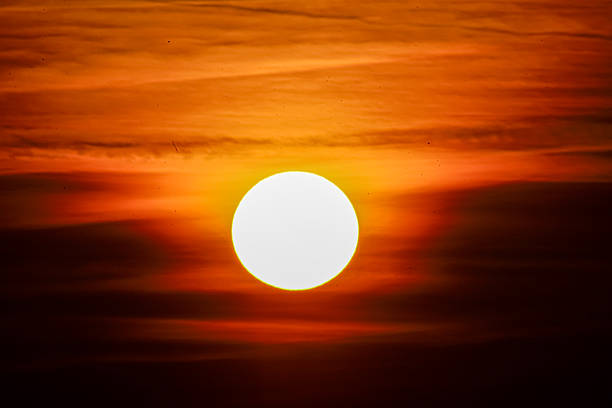 The sun is a brilliant white orb against a backdrop of fiery orange and red clouds, creating a breathtaking natural spectacle