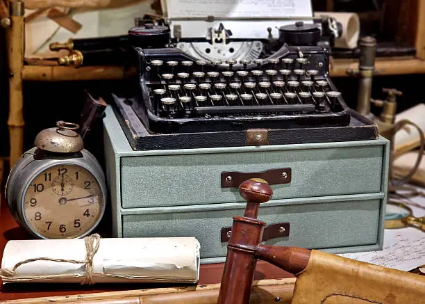 Photo of arrangement of historical objects that evokes atmosphere of an old study or museum. clock, alarm clock with bells and handle top winding spring. auction server or in antique bazaar. typewriter, pump
