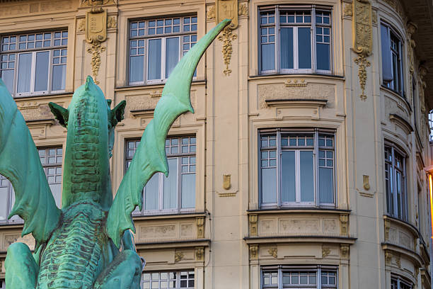 back side of the dragon statue on the Dragon Bridge, Ljubljana, back side of a green dragon statue on a historic city bridge, with an ornate building in the background.