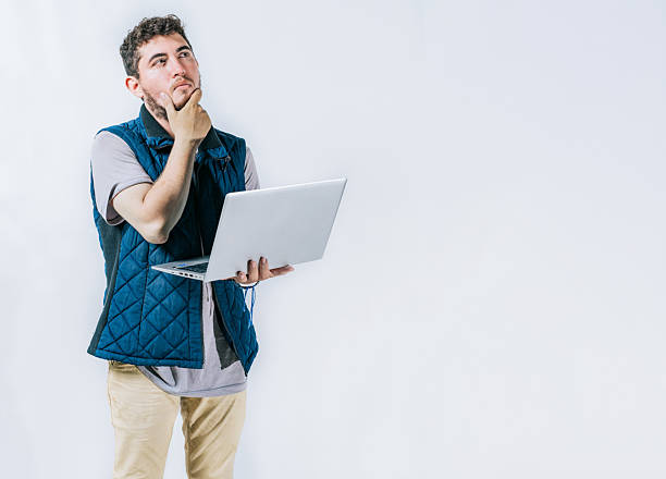 Asian man working on his laptop, looking stressed with his hand on his chin, thinking deeply about something