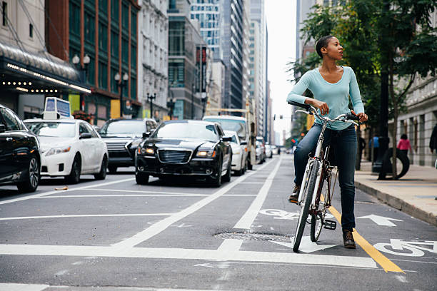 Female cyclist riding confidently through a city street with buildings and traffic in the background. This image conveys freedom, independence, and sustainable living in an urban environment.