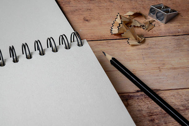 Top view of a blank spiral notebook with a pencil, sharpener, and pencil shavings on a wooden desk. Minimal study and planning concept with copy space, suitable for education, creativity, and note-taking themes.