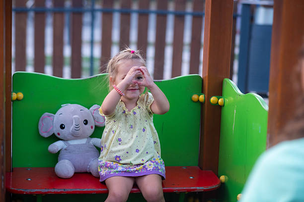 Little girl playing on playground, making a heart shape with fingers, showing love and joy