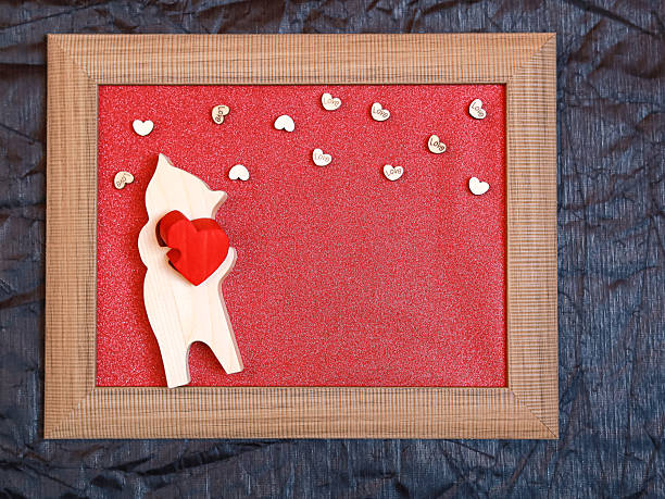 Wooden frame with romantic figurine and scattered heart symbols on a red background.Concept of Valentine's Day celebration, creative love messages, personalized greetings, and decorative romantic gifts.