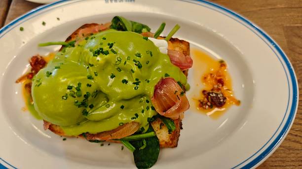 Gourmet breakfast plate with eggs benedict topped with green sauce, salmon, and fresh herbs served on toasted bread. The image represents healthy brunch, restaurant cuisine, food styling,