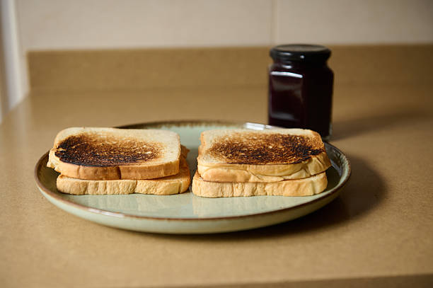A simple breakfast scene featuring two lightly charred toast slices on a plate with a jar of jam in the background, evoking cozy morning routine and homemade comfort.