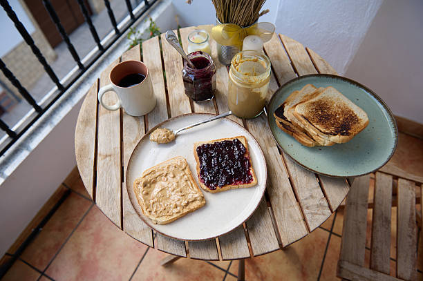 A relaxed morning scene on a wooden balcony table with toast, jam, peanut butter, coffee, and honey, creating warm, inviting breakfast vibes.