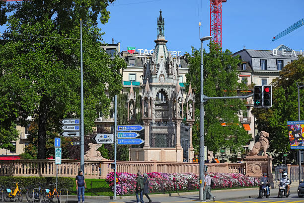 This image presents a stunning aerial perspective of Lausanne Cathedral, a prime example of Gothic architecture in Switzerland. Located in the city’s old town, the cathedral is framed by traditional terracotta-roofed buildings, urban structures, and Lake Geneva in the background. The nearby Alps enhance the scene’s natural grandeur. As a historical and cultural landmark, the cathedral dominates Lausanne’s skyline, combining spiritual heritage and architectural elegance. Captured on a bright summer day, the image represents Swiss identity and the beauty of urban and natural harmony.