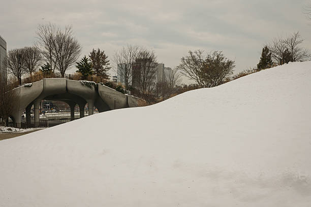 Little Island, a public park built on Pier 55 along the Hudson River, is seen in New York City during winter. The park features an elevated landscape supported by sculptural concrete columns, with views of the Manhattan skyline and the river.