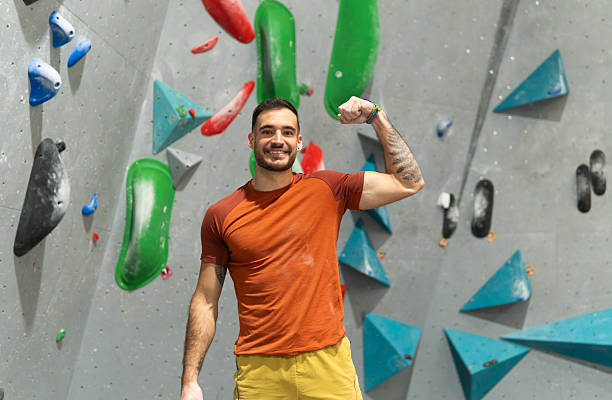 Happy man flexing arm muscles showing strength at a bouldering gym