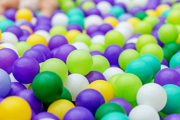 Vibrant mix of green, purple, yellow, teal, and white plastic balls in an indoor ball pit used for childrenâs sensory play.