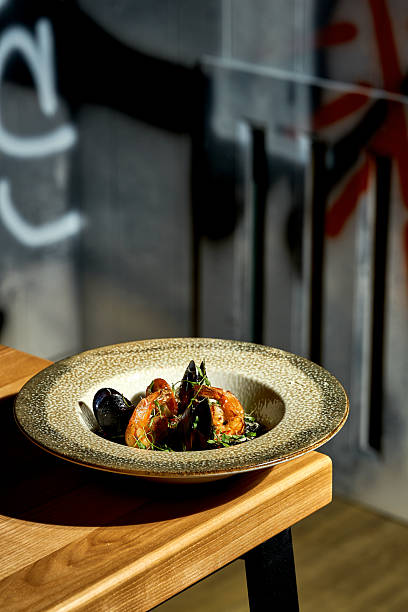 A professional, high-angle studio shot of a gourmet black seafood risotto (Arroz Negro) elegantly served in a deep blue ceramic bowl.