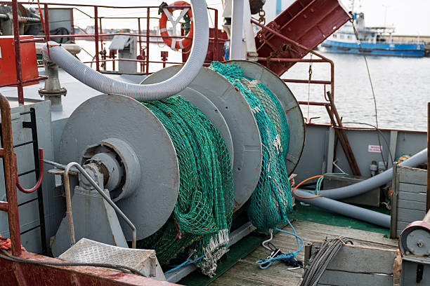 Large metal reels holding green industrial fishing nets on the deck of a commercial boat. The scene depicts maritime industry and professional fishing equipment in a harbor setting.
