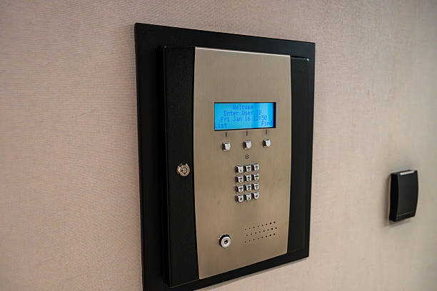 A wall-mounted, keypad-operated electronic safe with an integrated digital display. The safe features a modern design, combining black and silver tones, and has both keypad and key access.