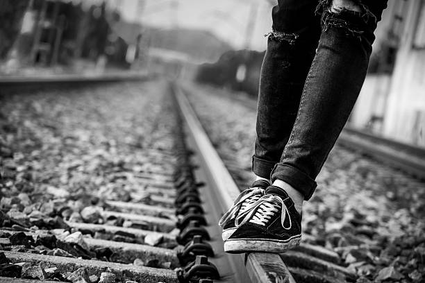 Black and white photo of a person walking and balancing on a railway track. Urban lifestyle concept with shallow depth of field and selective focus