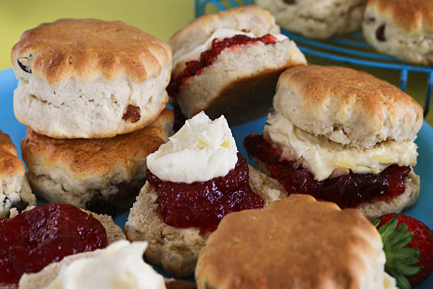 Image of freshly baked raisin scones on plate and cooling rack, served with clotted cream, strawberry jam, and fresh strawberries