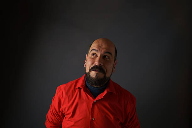 A confident bald man with a goatee, dressed in a red shirt, poses directly at the camera against a dark, minimalistic background. The image highlights strong personality, modern style, and professional portrait aesthetics, perfect for lifestyle, business, or creative stock content.