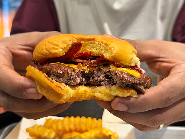Image of person enjoying a bite while eating fries and cheeseburger beef burger hamburger with melted cheese and crispy bacon