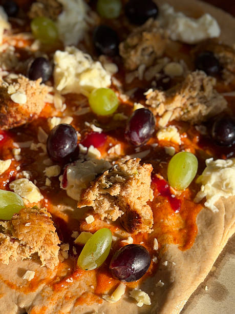 Image of uncooked homemade pizza with savory sausages, fresh grapes, and melted mozzarella cheese on dough base